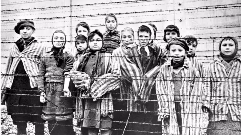 A group of child survivors behind a barbed wire fence at the Nazi concentration camp at Auschwitz